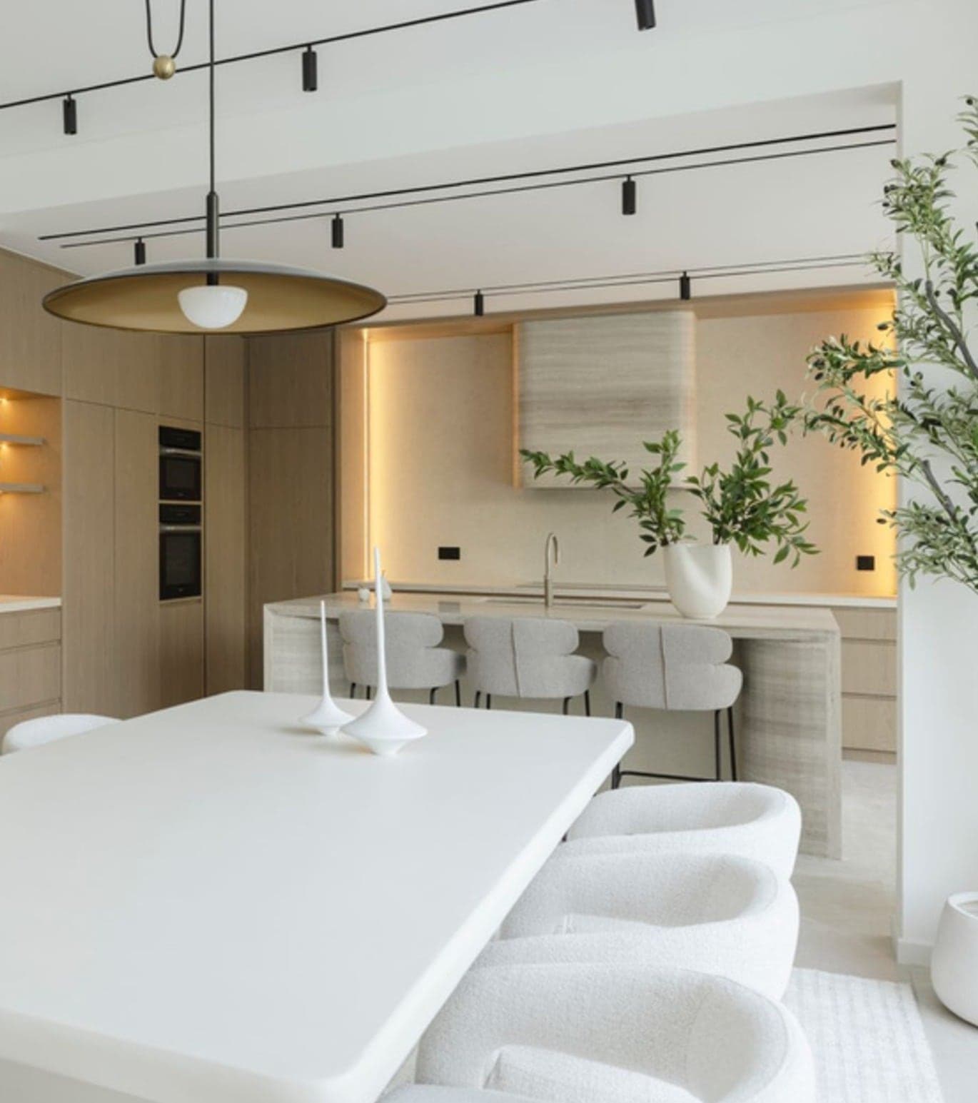 Open-plan kitchen and dining room in pale oak with a sculptural white table and brass pendant